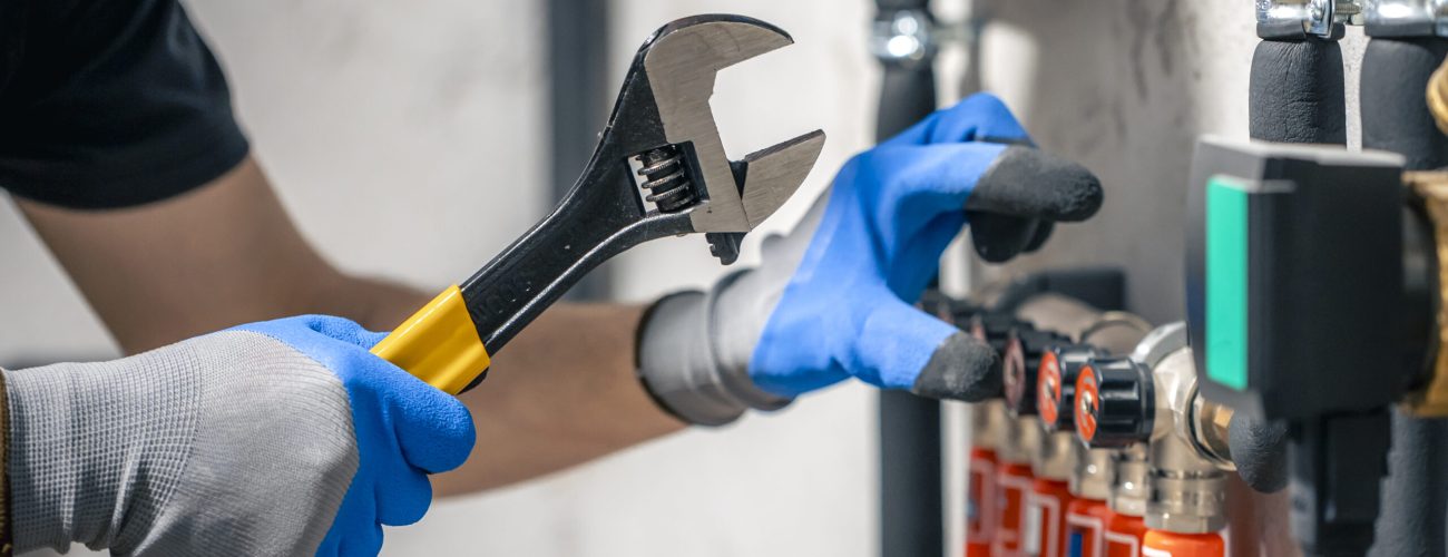A man installs a heating system in a house and checks the pipes with a wrench. Adjusting heating valves in a residential building. A plumbing and heating technician works.